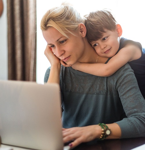 photograph of a mother working on a laptop and her child